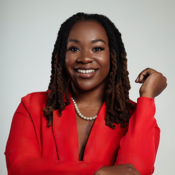Photo of Ashley Ewings, an African-American woman. In the photo Ashley's hair is braided, smiling, and wearing a red blazer.