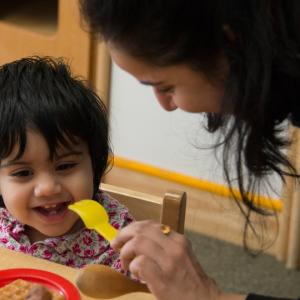 Woman holding a fork and showing to smiling toddler