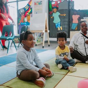 adorable black children sitting on a playmat in a preschool setting, along with black educators. 