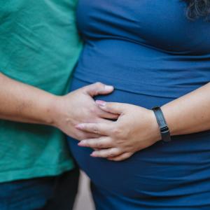 A pregnant woman and her partner. His hand is on her belly, and her hand is over his. 